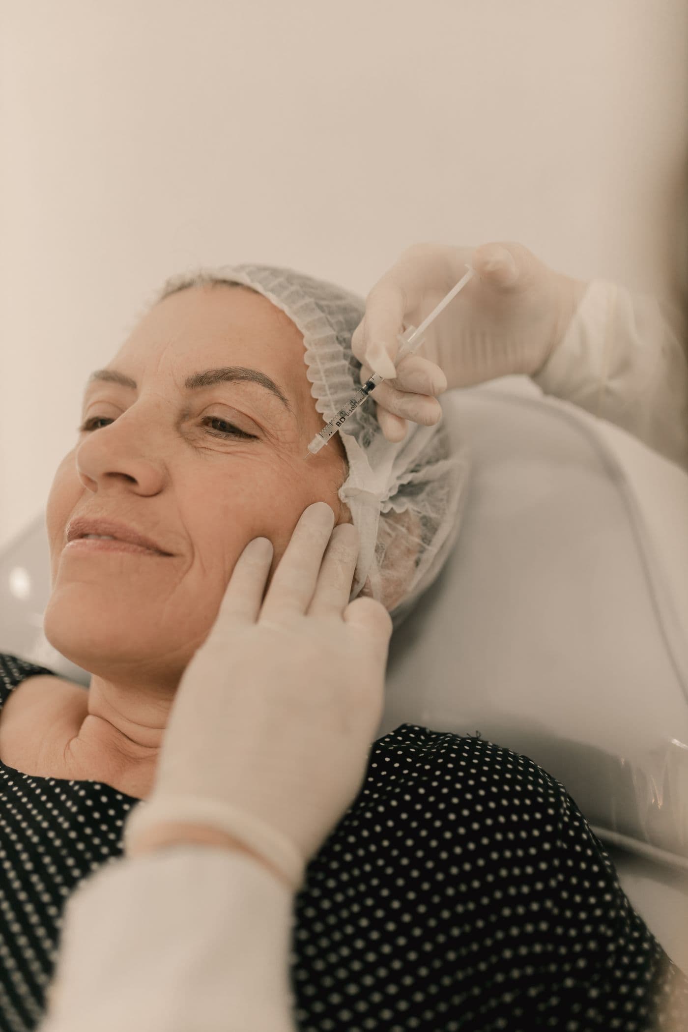 Mature woman reclining as a practitioner places micro-injections along her cheek