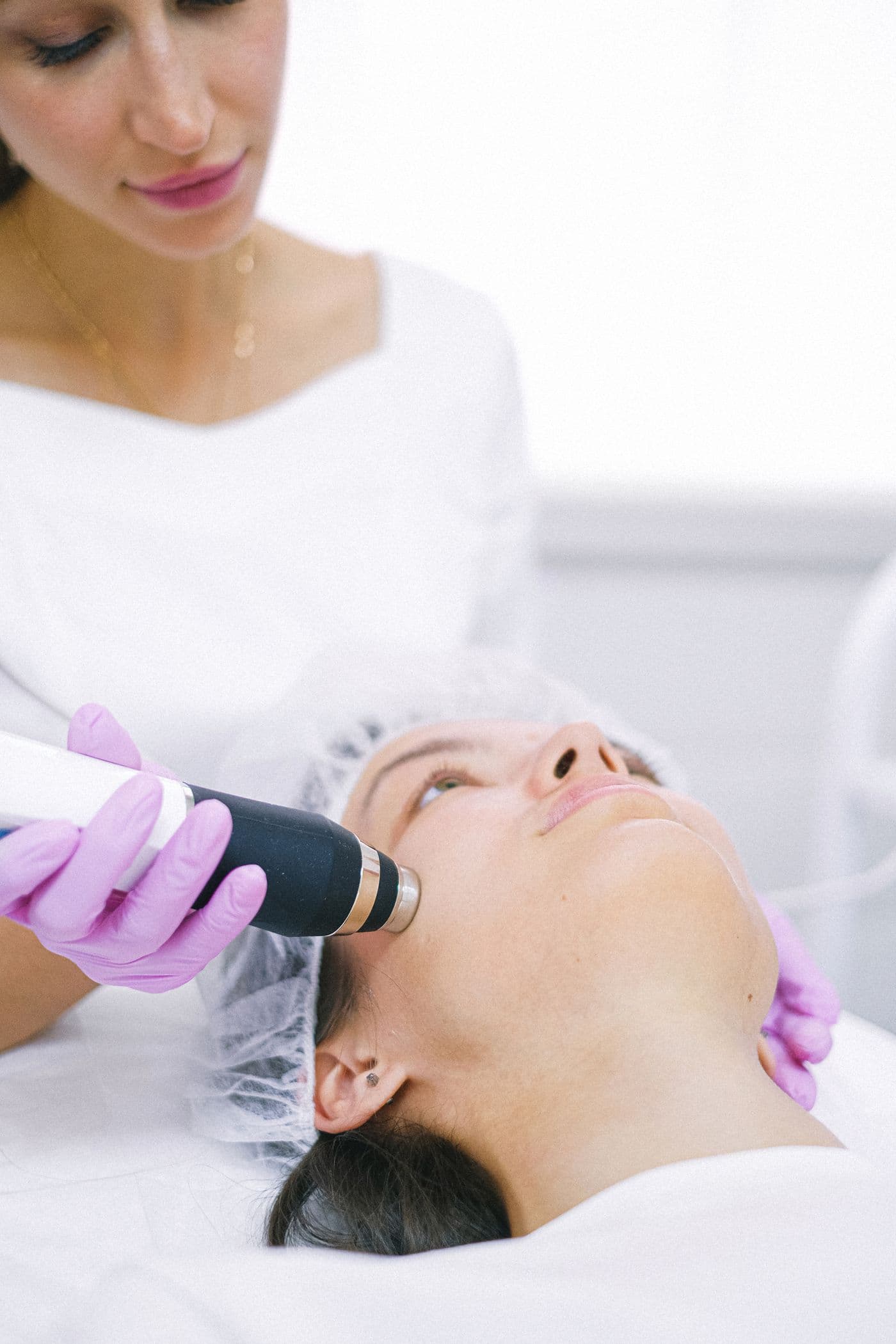 Practitioner in gloves holding a light-based device over a patient's face