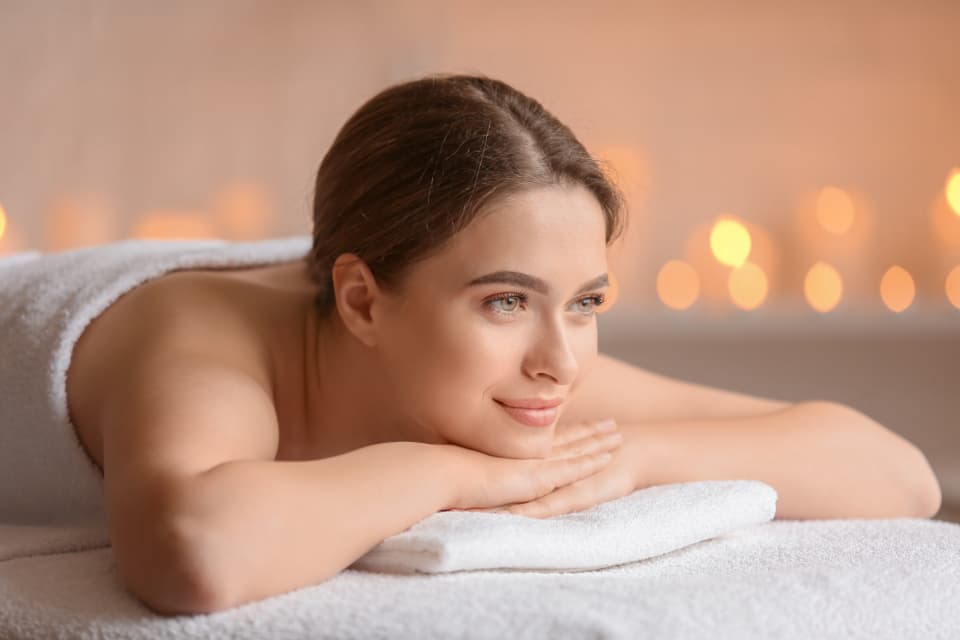 Woman resting on a treatment bed in a candlelit spa room